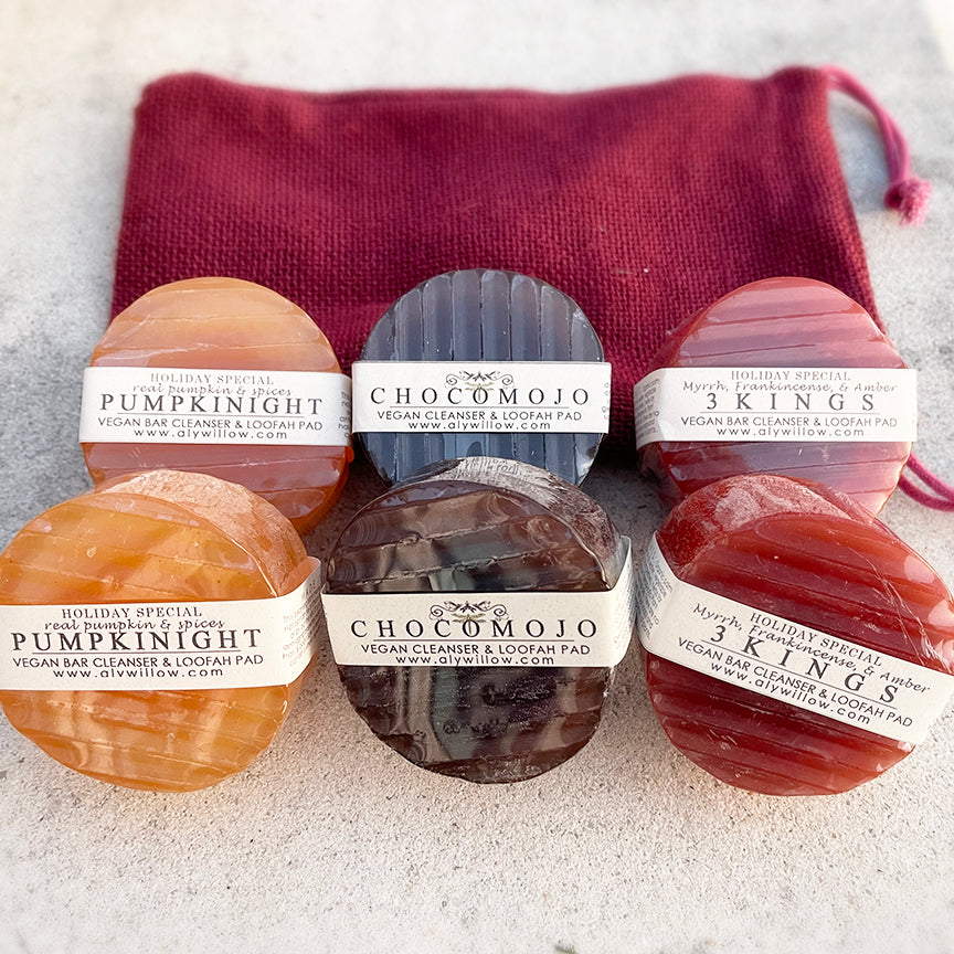Three different colored bars of soap labeled as Pumpkinight, Choomojo, and 3KINGS, each with a unique scent, displayed in front of a burgundy textured bag.
