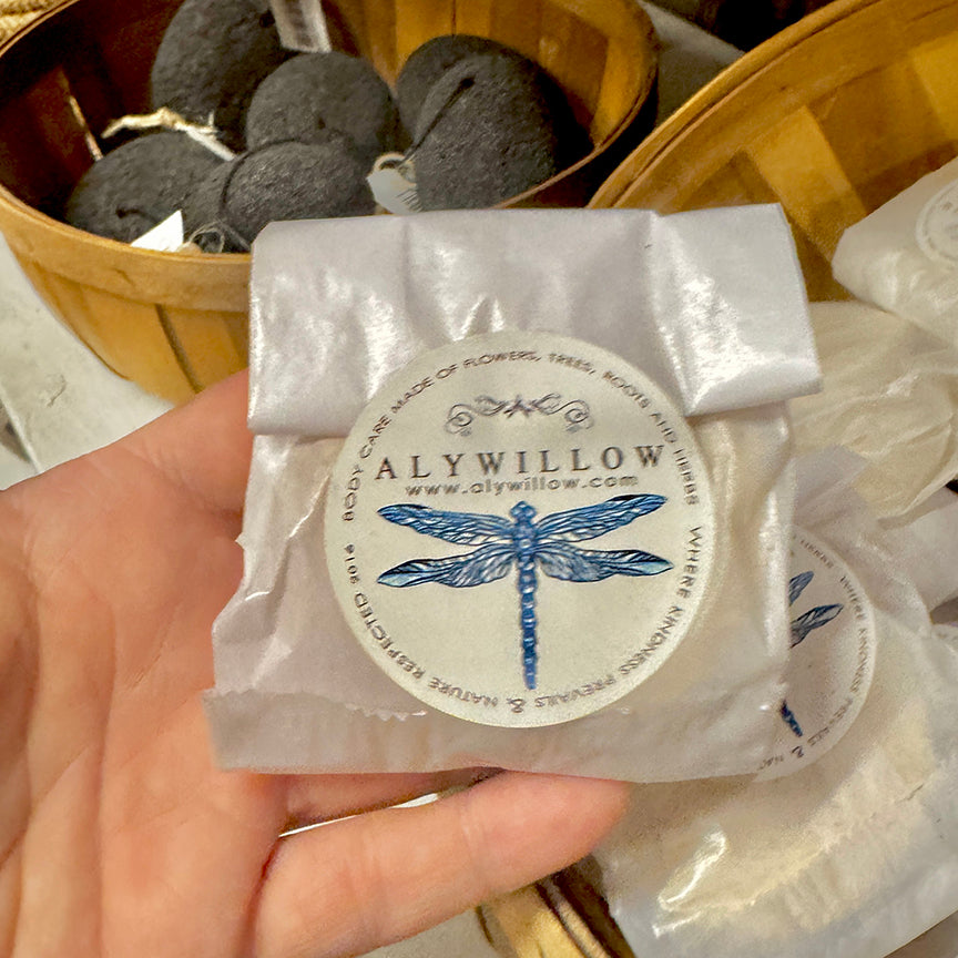 Hand holding a wrapped product with Alywillow branding and a dragonfly design.