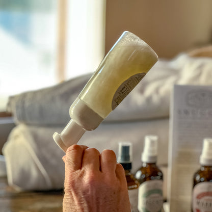 Hand flipping a bottle of Unscented UDC with a blurred background of bottles and a box.